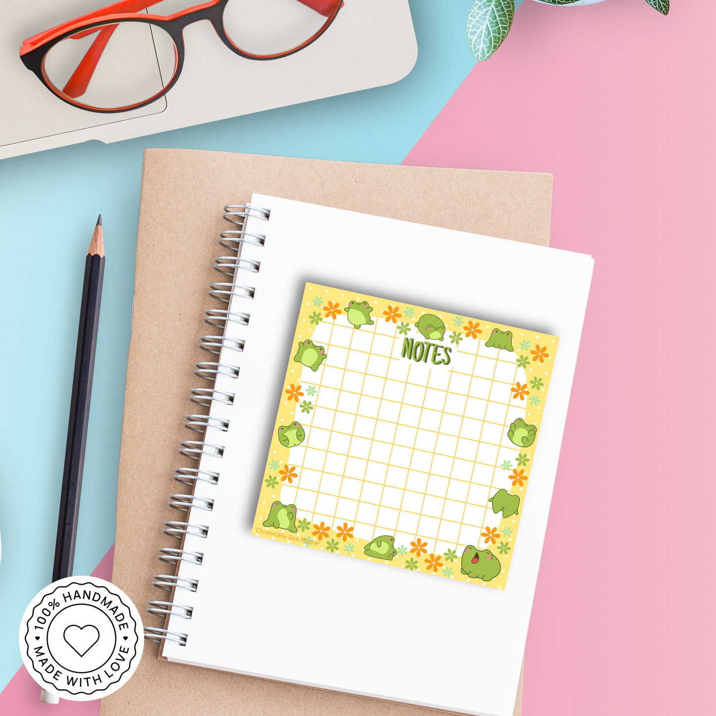 Notebook with a decorative sticky note featuring frogs and the word 'Notes', on a colorful background.