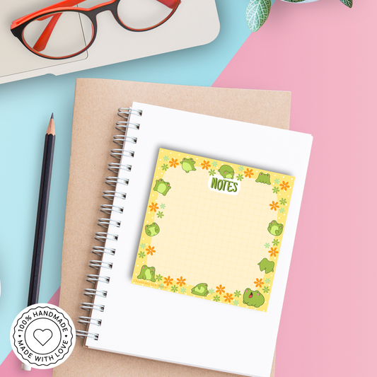 Notebook with a sticky note featuring frog illustrations on a colorful background