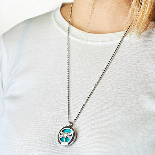 Person wearing a necklace with a circular pendant on a plain Dragon Fly background